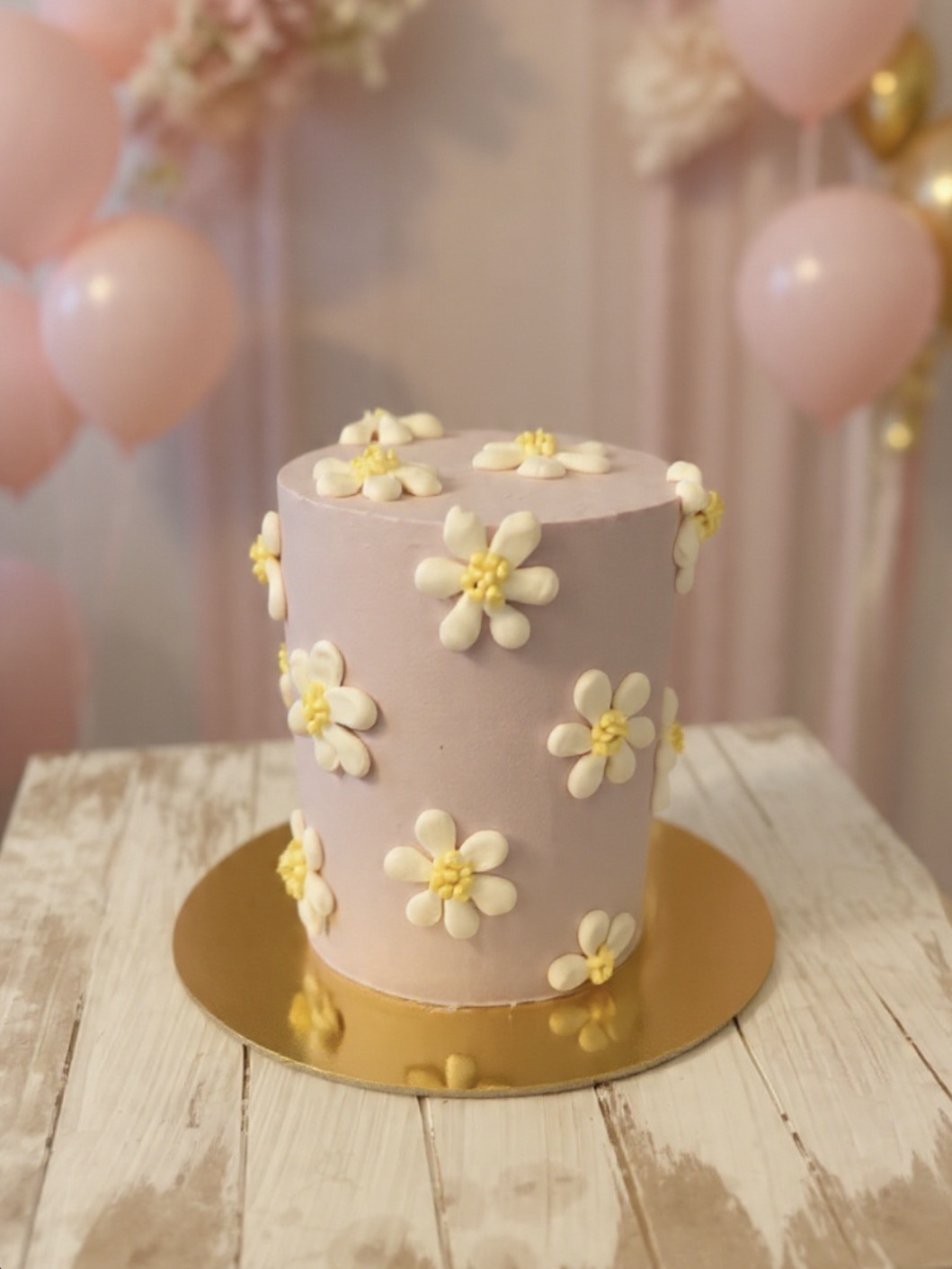 Blush daisy cake and soft pink balloons styled with a painterly hand